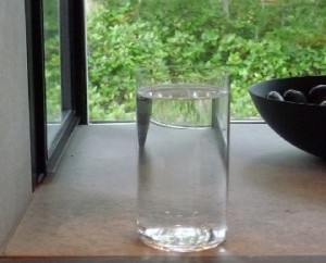Glass of water on windowsill with greenery.